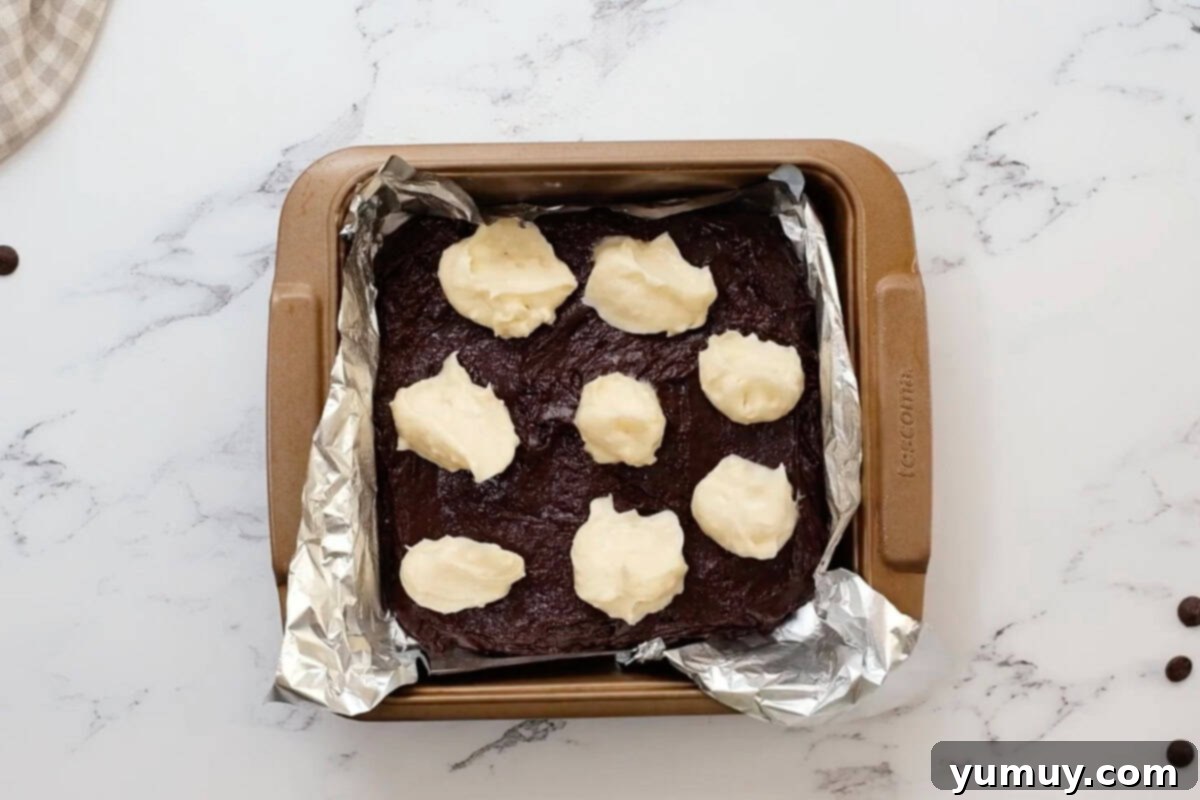 dollops of sweetened cream cheese over brownie batter in a foil-lined baking pan.