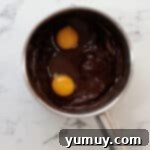 adding two eggs to melted chocolate and butter in a saucepan.