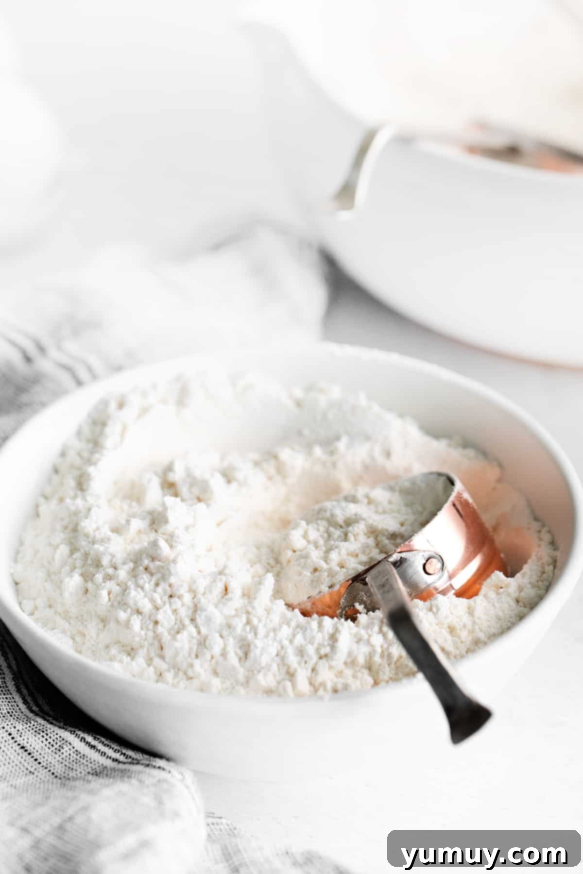 A bowl of freshly prepared homemade cake flour, ready for use, with a measuring cup beside it, illustrating the ease of preparation.