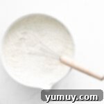 A whisk gently resting in a bowl filled with flour, ready to begin the sifting process.