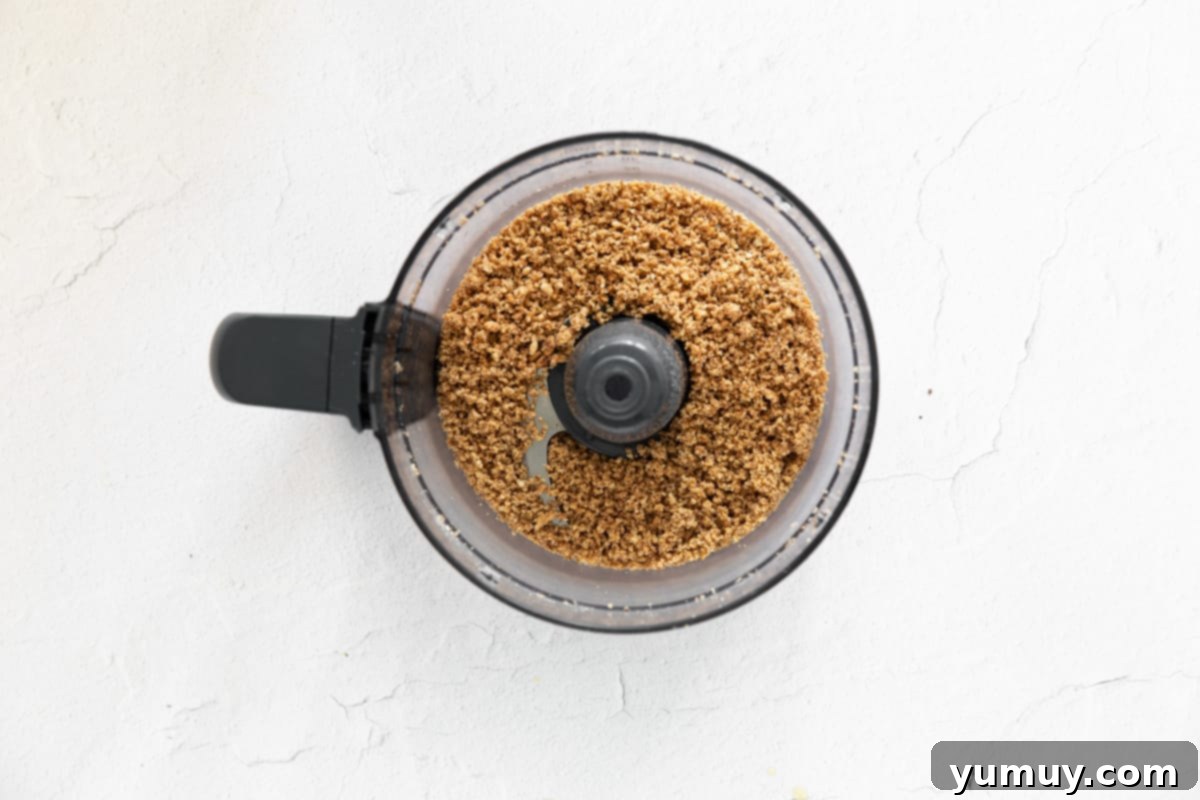 Velvety Homemade Chocolate Hazelnut Spread 9 A close-up shot of a layer of finely ground hazelnuts in a food processor, appearing like a coarse meal, a crucial step in making homemade Nutella.