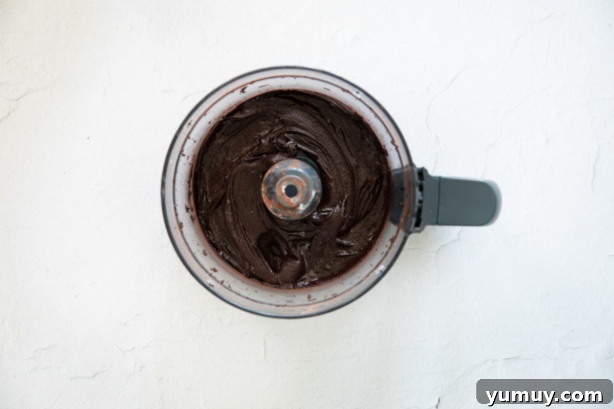 Velvety Homemade Chocolate Hazelnut Spread 10 Close-up of all homemade Nutella ingredients, including chocolate, oil, and sugar, actively blending in a food processor to create a smooth, rich spread.