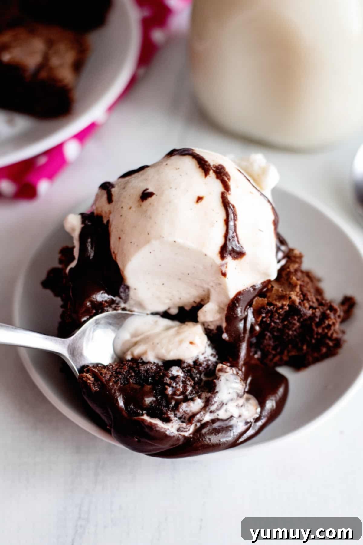 Decadent Chocolate Fudge Sauce 3 A delectable dessert scene: a generous scoop of vanilla ice cream, flanked by a rich brownie, all lavishly coated with homemade hot fudge sauce, ready to be enjoyed.