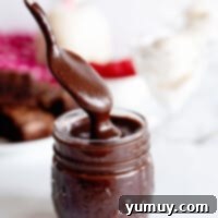 Decadent Chocolate Fudge Sauce 4 A spoon dipping into a jar of homemade hot fudge, illustrating its thick, glossy texture, ready to be served over desserts.
