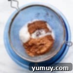 Decadent Chocolate Fudge Sauce 5 Dry ingredients being sifted into a bowl, forming a neat pile of cocoa, sugar, and spices, key for a lump-free hot fudge sauce.