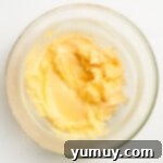 Creaming butter, powdered sugar, and lemon zest in a glass bowl on a white surface using a hand mixer.