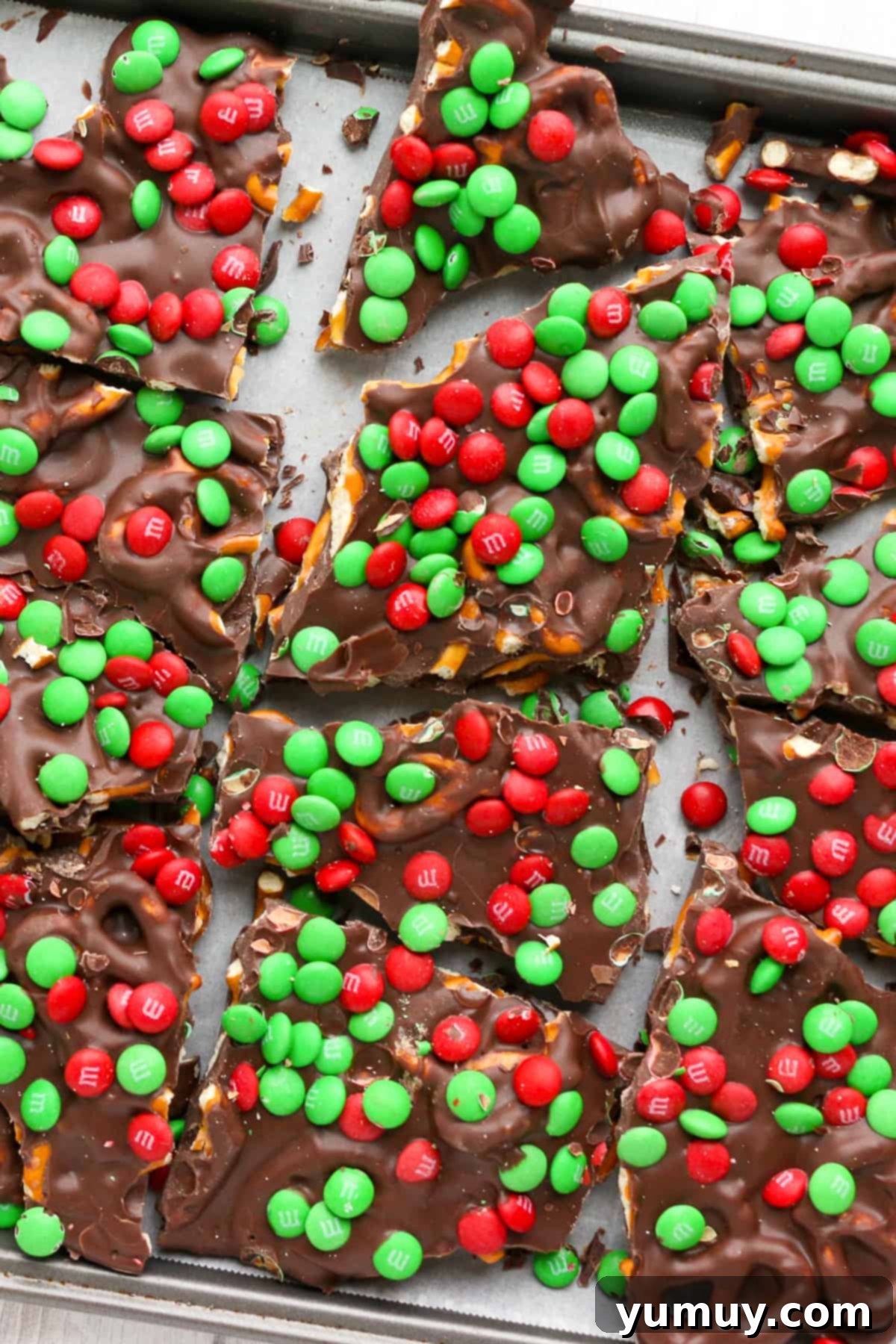 Festive Pretzel Bark 2 Close-up of vibrant M&M Christmas pretzel bark on a baking sheet, showcasing colorful candies and glistening chocolate.