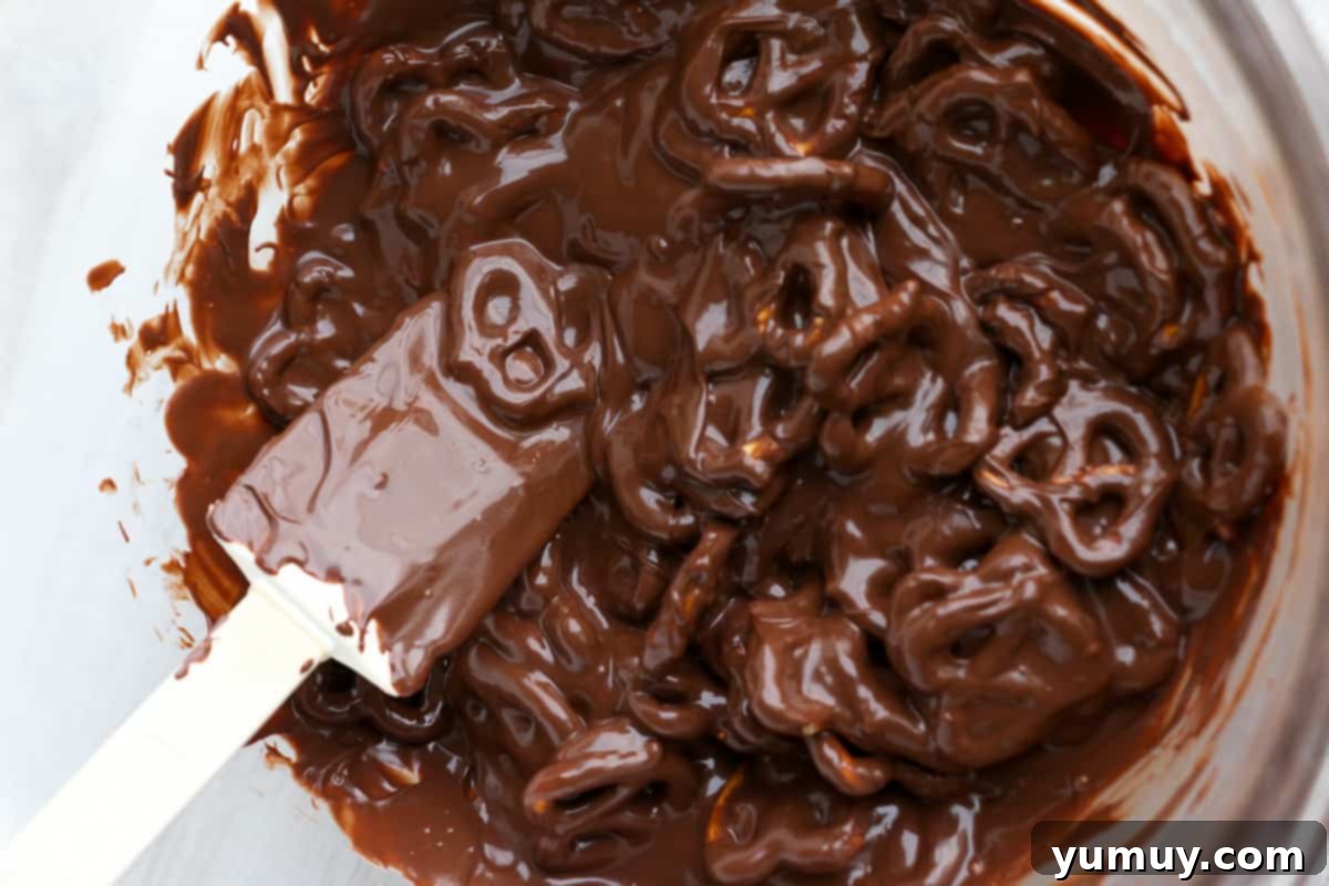 Festive Pretzel Bark 10 Visual guide: Mixing pretzels into melted chocolate with a spatula on a baking sheet.