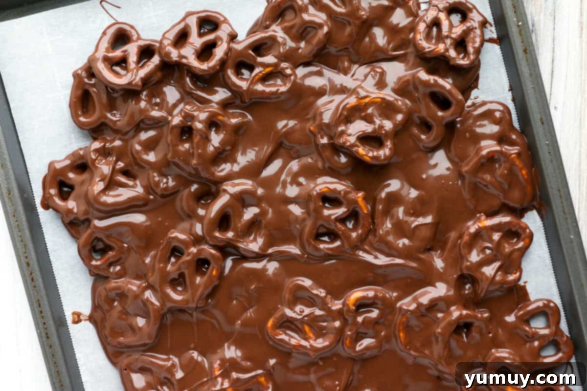 Festive Pretzel Bark 11 Visual guide: Spreading the chocolate pretzel mixture onto parchment paper on a baking sheet.