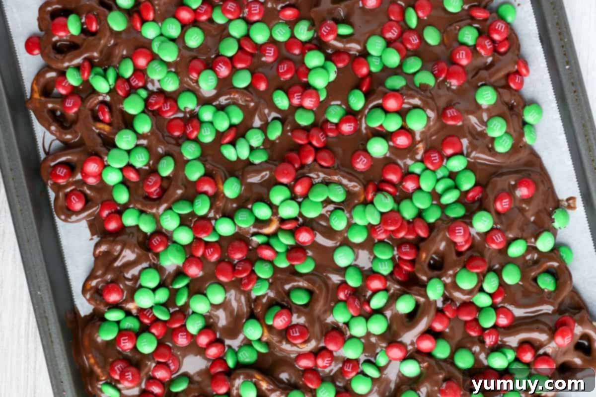 Festive Pretzel Bark 12 Visual guide: Sprinkling red and green Christmas M&M's over the chocolate pretzel base.