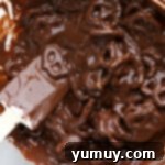 Festive Pretzel Bark 6 Pretzels being coated in melted chocolate in a bowl using a rubber spatula.