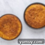 Two golden-brown cake layers in round pans cooling on a wire rack.
