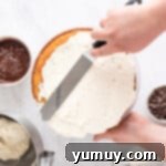 A baker using an offset spatula to apply frosting evenly on the side of a cake layer.