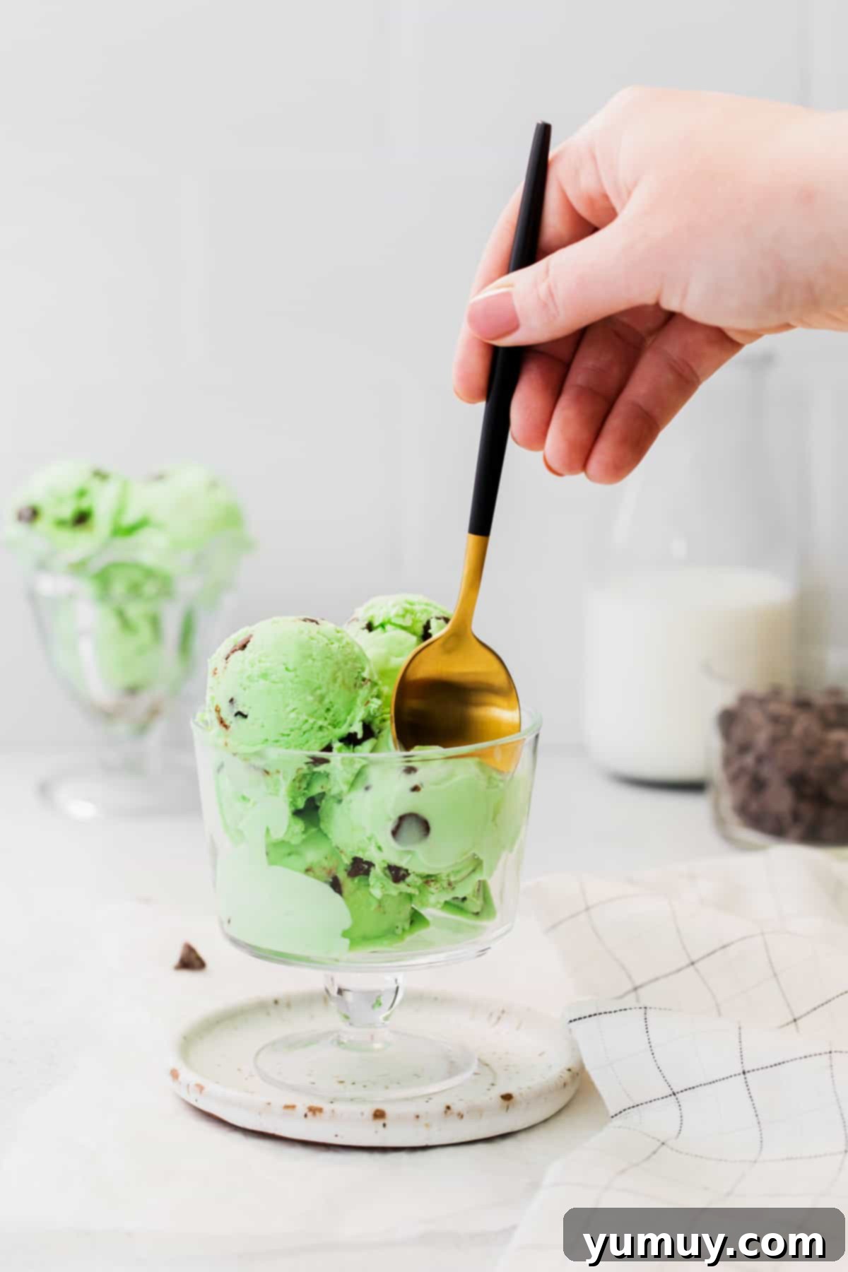 No-Churn Mint Chip Bliss 2 A hand expertly digging a spoon into a cup of homemade no-churn mint chocolate chip ice cream, highlighting its creamy texture and abundant chocolate chips.