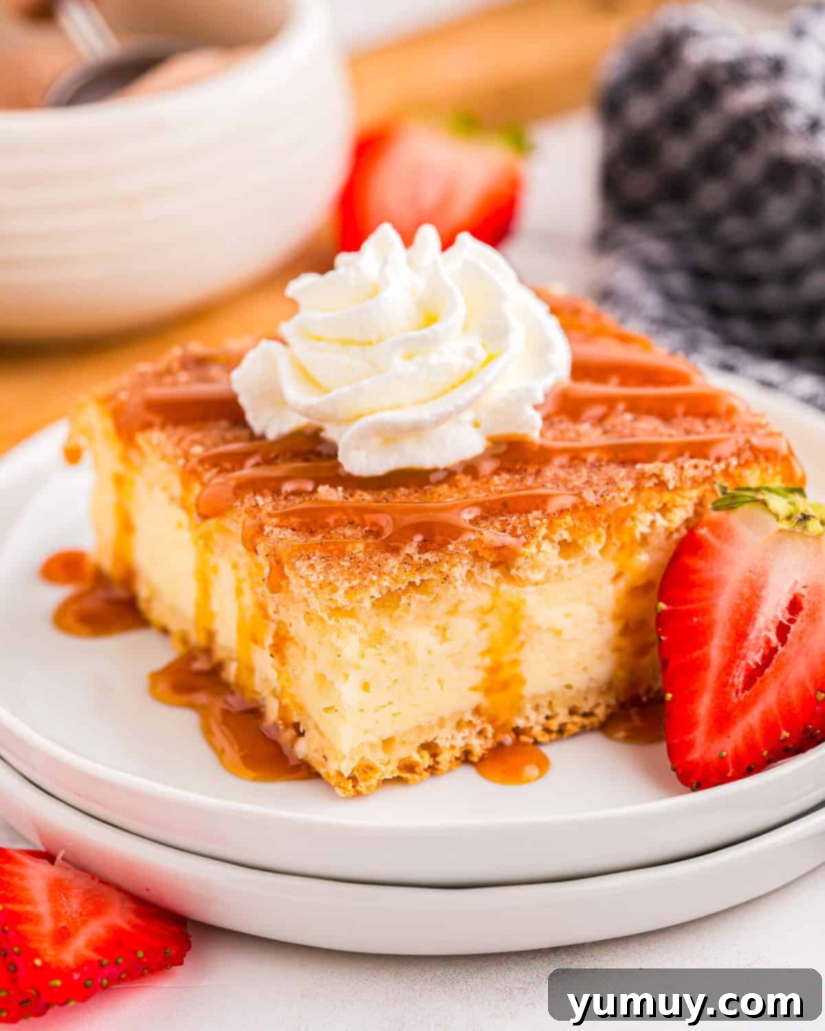 A churro cheesecake bar on a white plate with whipped cream, caramel sauce, and strawberries, ready to be enjoyed.