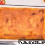 Baked churro cheesecake bars glistening with a caramelized cinnamon sugar topping in a rectangular baking dish, fresh from the broiler.