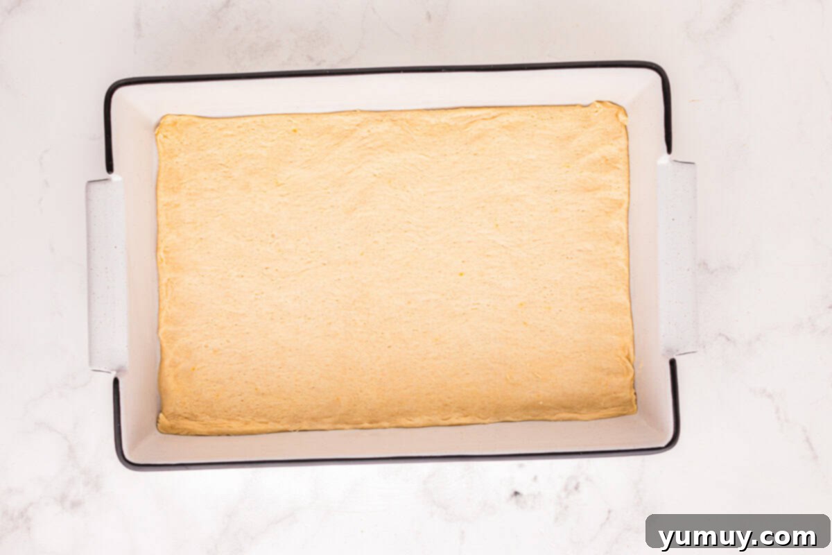 Crescent dough sheets expertly pressed into a rectangular baking pan, forming the foundational layer of the churro cheesecake.
