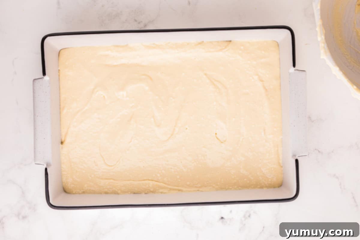 Smooth cheesecake filling evenly spread over the crescent roll dough base in a rectangular baking pan.