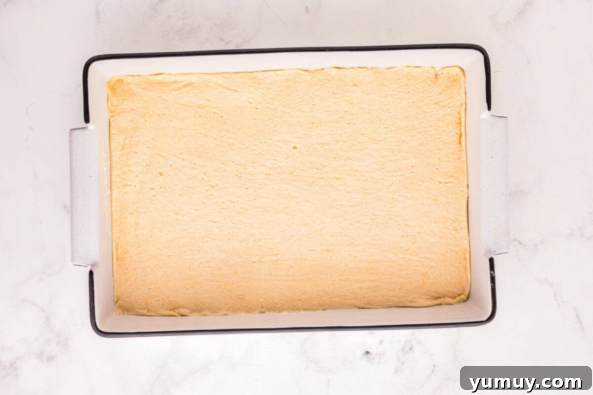 An unbaked churro cheesecake, with the second layer of crescent dough perfectly covering the creamy filling in a rectangular baking pan.