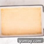 Unbaked churro cheesecake bars, with the top crescent dough layer perfectly placed over the filling, in a rectangular baking pan.