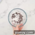 Semisweet chocolate chips and heavy cream combined in a glass bowl, ready for microwaving to create ganache.