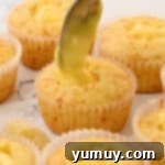 Pastry cream being carefully spooned or piped into the cored centers of baked cupcakes.