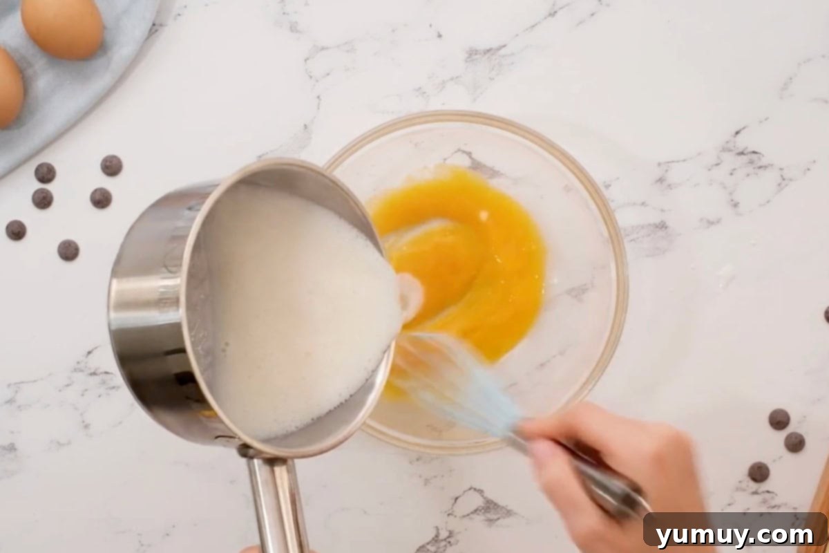 The process of tempering, where warm milk mixture is slowly poured into whisked egg yolks.