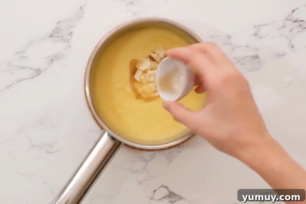 Adding butter and vanilla to the hot pastry cream in a saucepan, stirring until smooth.