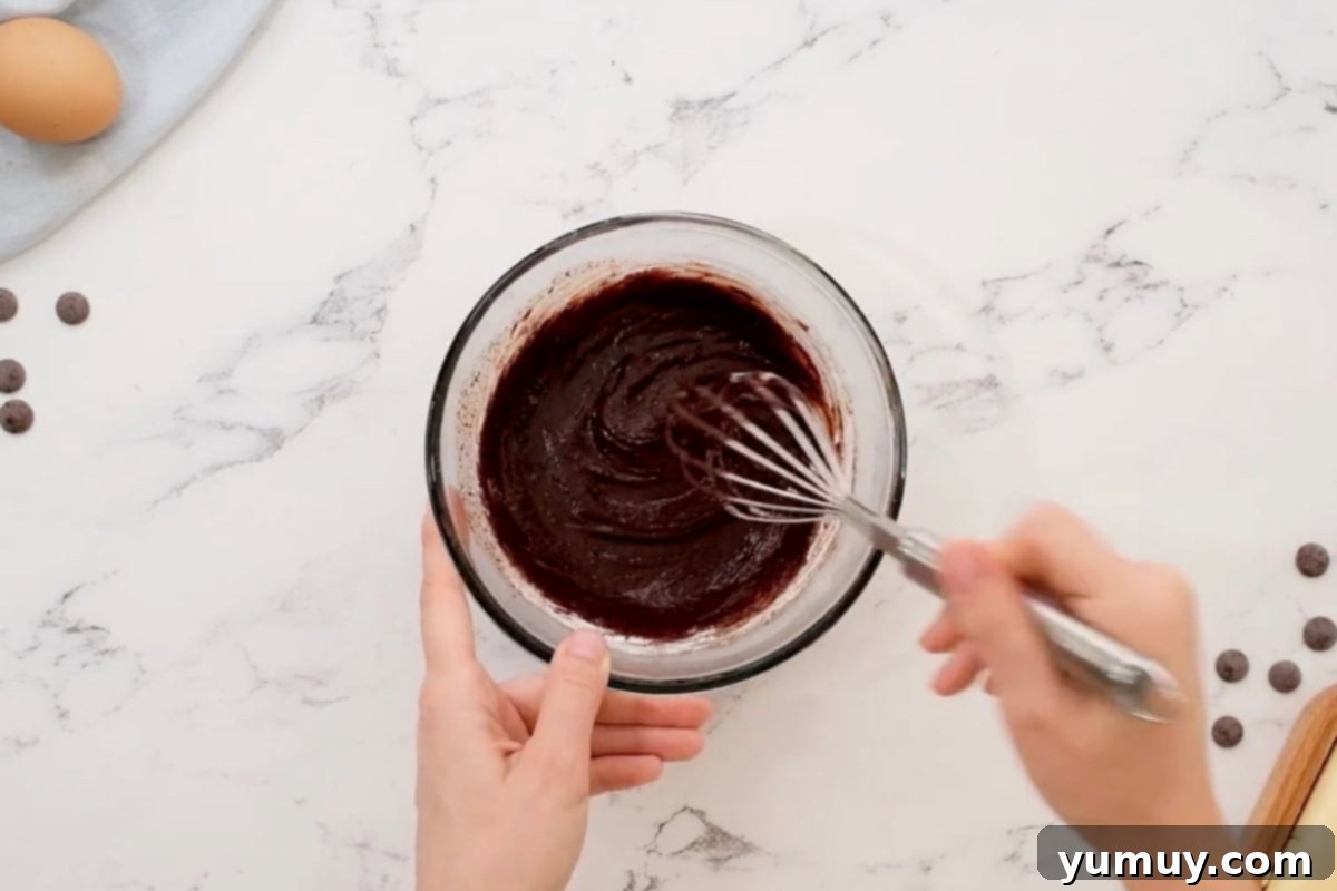 Thickened and glossy chocolate ganache being whisked in a glass bowl.