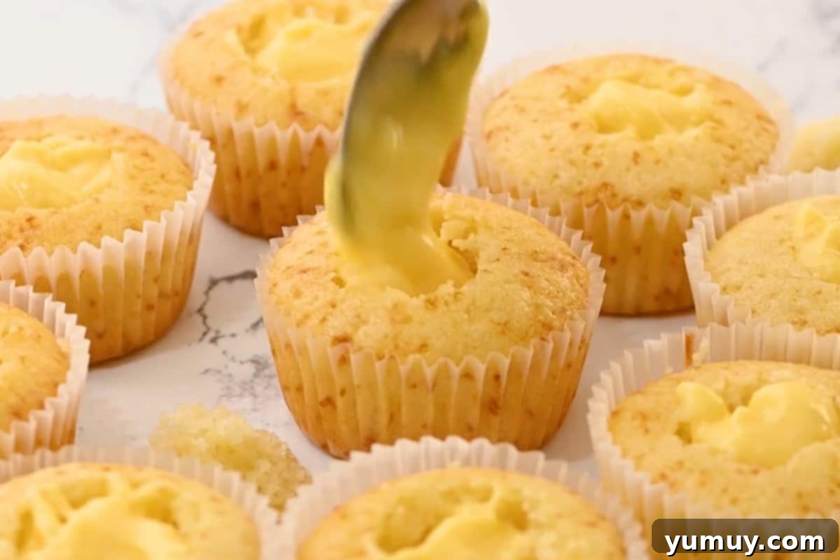 Spoonfuls of rich pastry cream being placed into the cored centers of cupcakes.