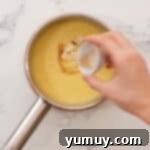 Unsalted butter and vanilla extract being added to the hot pastry cream in a saucepan and stirred until smooth.