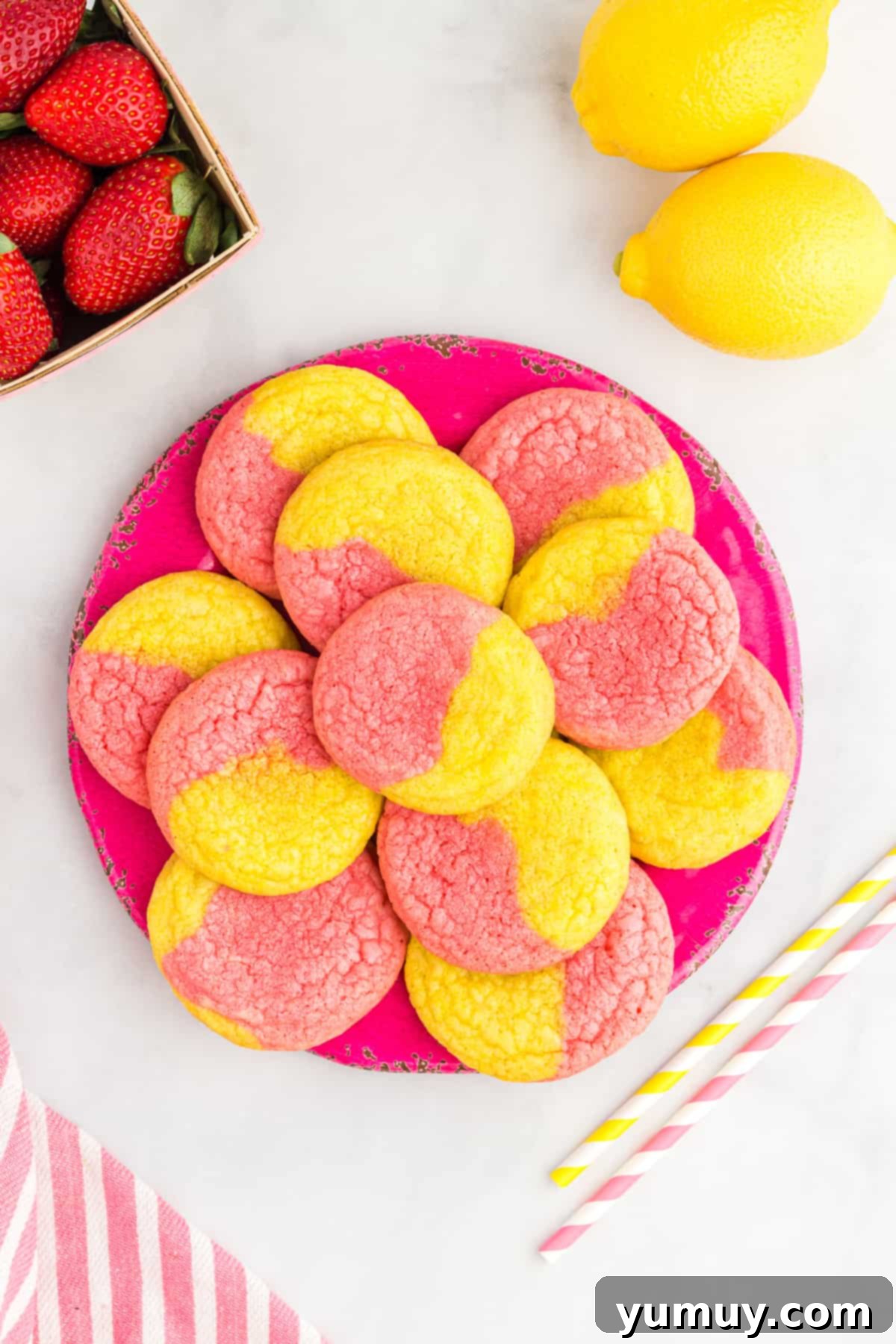 Pink and yellow swirl strawberry lemonade cookies on a serving plate, garnished with fresh strawberries and lemon slices.