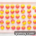 Swirled pink and yellow cookie dough balls lined up on a parchment-lined baking sheet.