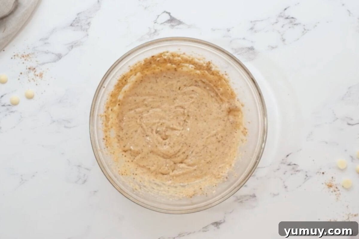 Egg and vanilla extract being added to the creamed butter and sugar mixture in a glass bowl.