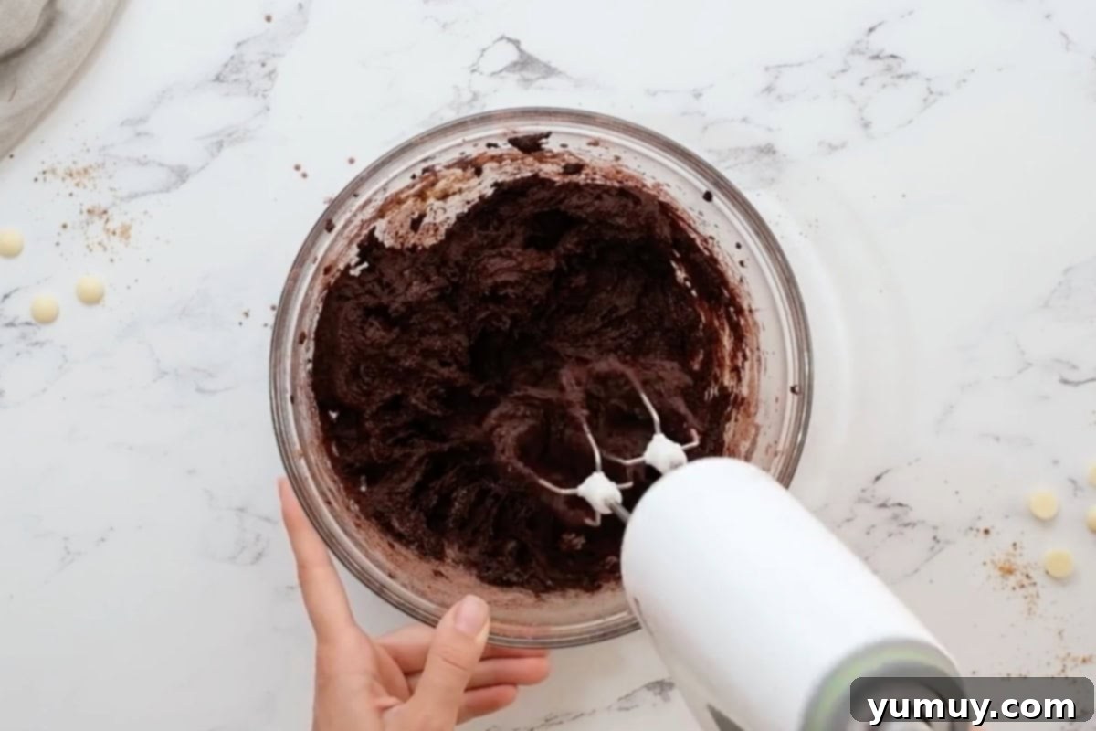 Thick chocolate cookie dough being mixed with milk in a glass bowl.