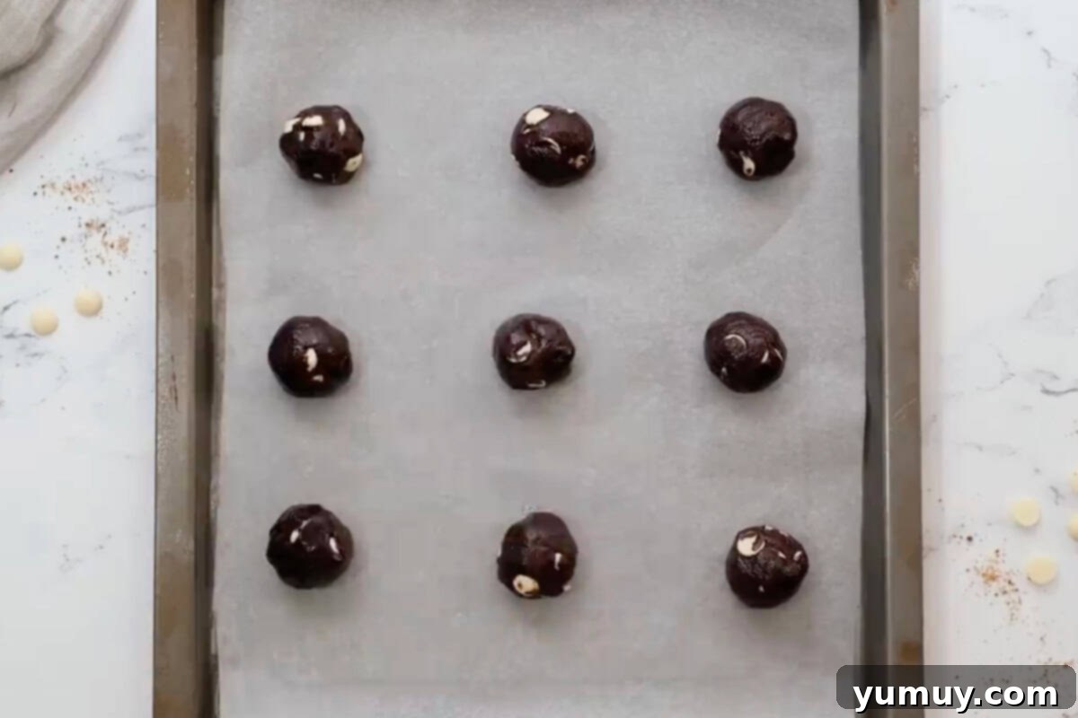Portioned chocolate white chocolate cookie dough balls neatly arranged on a parchment-lined baking sheet.