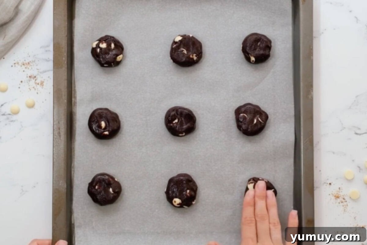Gently pressing chocolate white chocolate chip cookie dough balls flat on a baking sheet before baking.