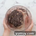 Chocolate white chocolate chip cookie dough in a glass bowl covered with plastic wrap, chilling.