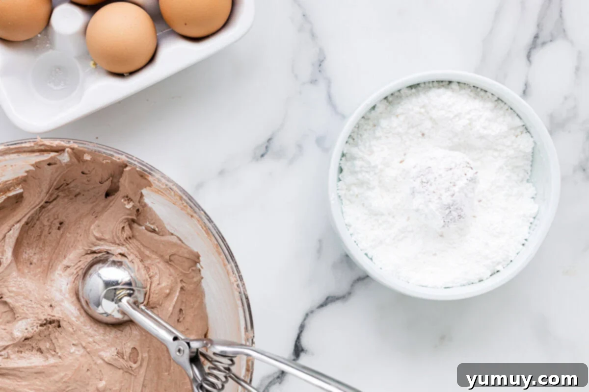 Cool Whip Cloud Cookies 11 A coated chocolate cookie dough ball resting in a bowl of powdered sugar, ready for baking.
