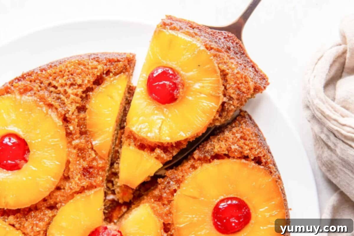 Last Hurrah of Summer Desserts 5 Close-up, overhead view of a perfect slice of golden Pineapple Upside Down Cake, glistening with caramelized pineapple and cherries, being carefully lifted from a pan with a cake server.