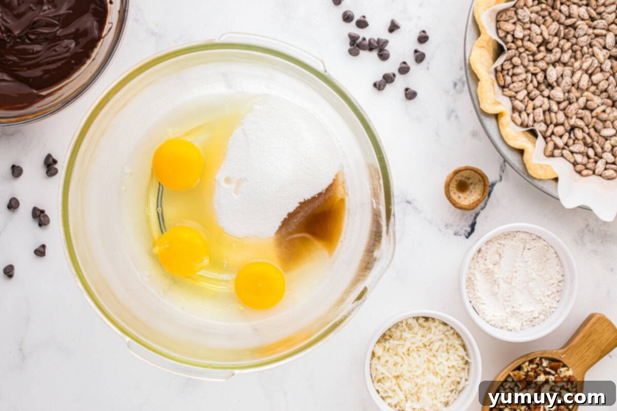 German Chocolate Coconut Pecan Delight Pie 19 A clear glass bowl holding whisked eggs, granulated sugar, and vanilla extract, appearing light and slightly frothy.
