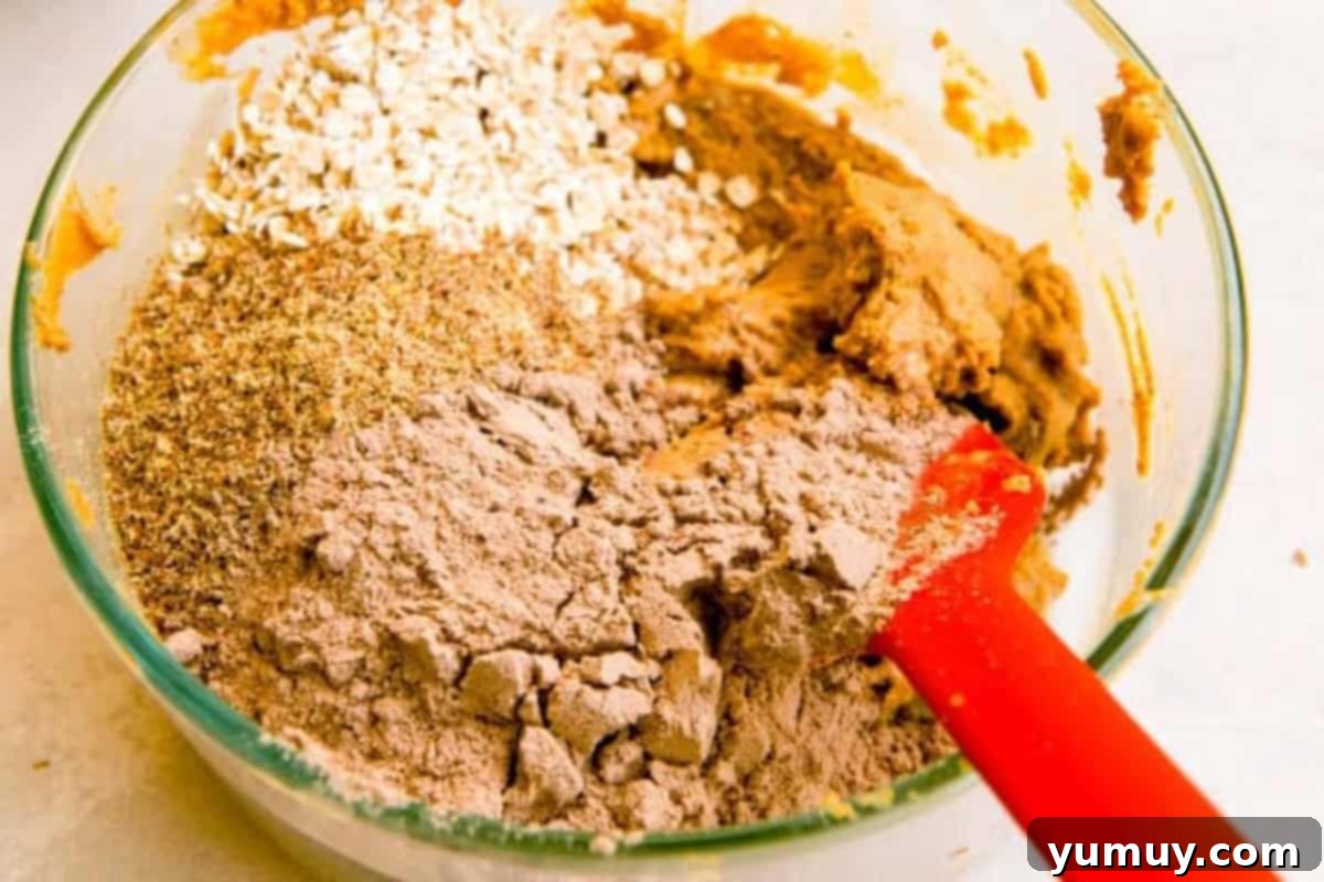 Crafting Your Perfect Protein Bars 9 oats, nuts, protein powder, nut butter, and more in a glass mixing bowl with a red rubber spatula.