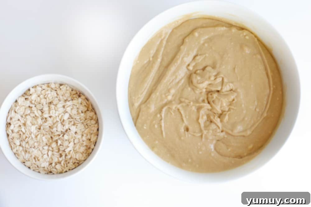 Overhead view of cookie batter in a large bowl, with oats awaiting incorporation.