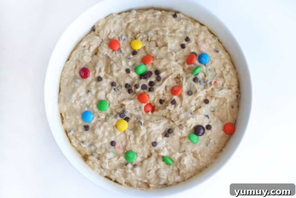 Monster cookie dough in a mixing bowl, covered and chilling in the refrigerator.