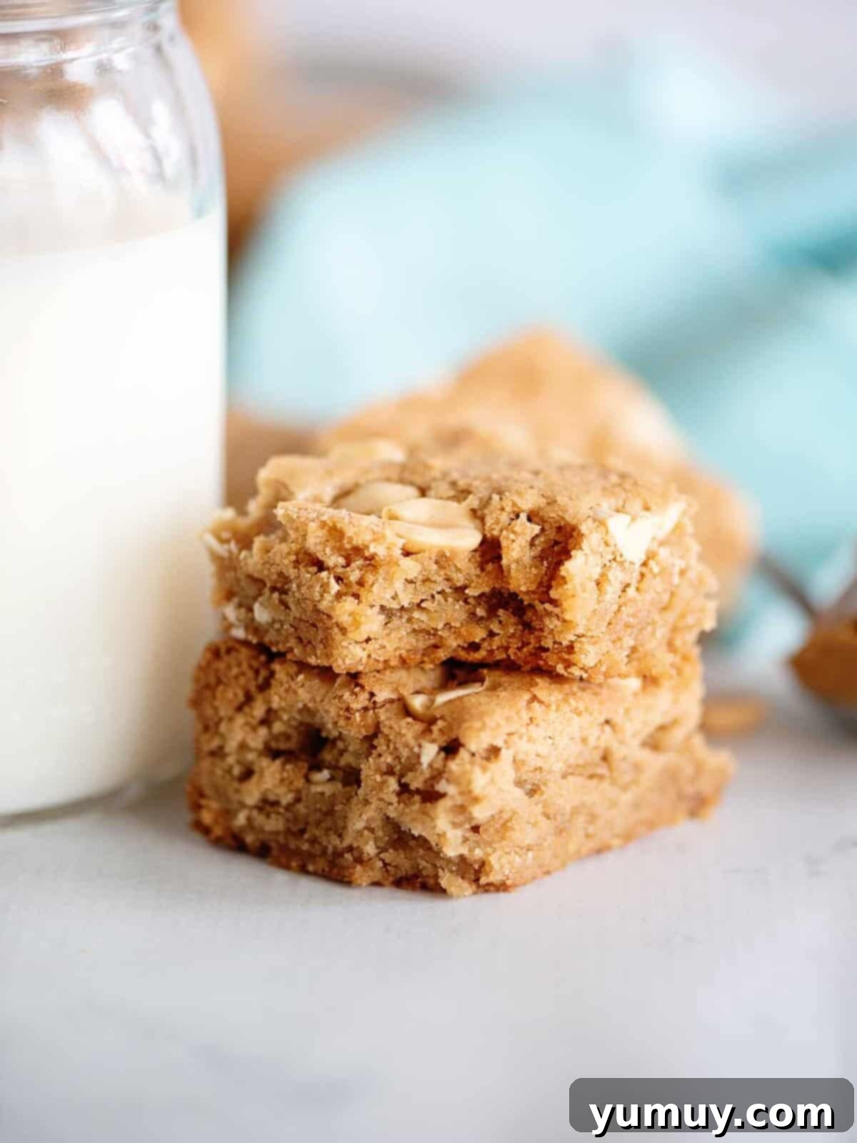 Two chewy peanut butter blondies stacked, one with a bite taken, showcasing its soft texture
