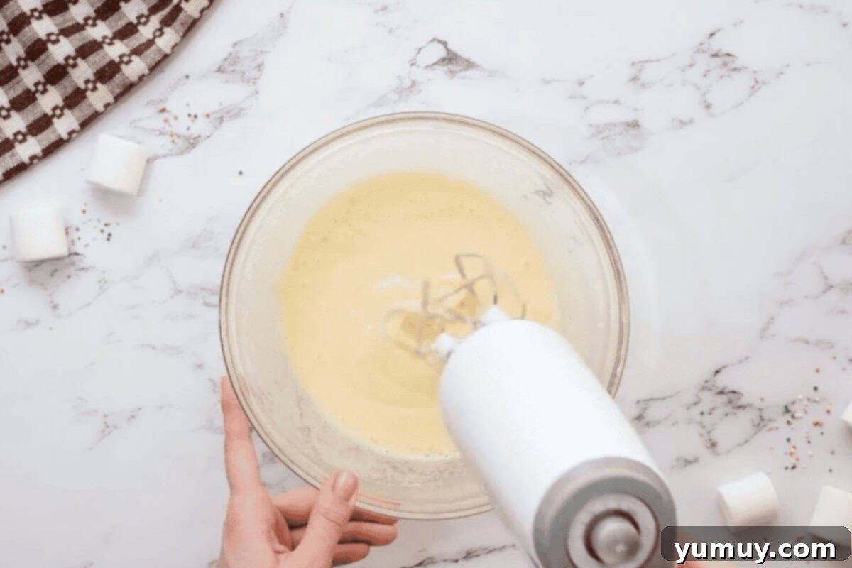 beating sugar, eggs, and vanilla in a glass bowl with a hand mixer.