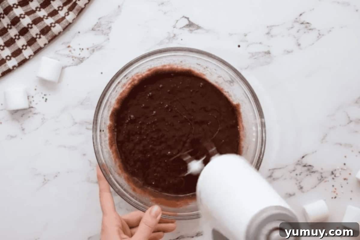 beating wet ingredients for hot chocolate cookies in a glass bowl with a hand mixer.