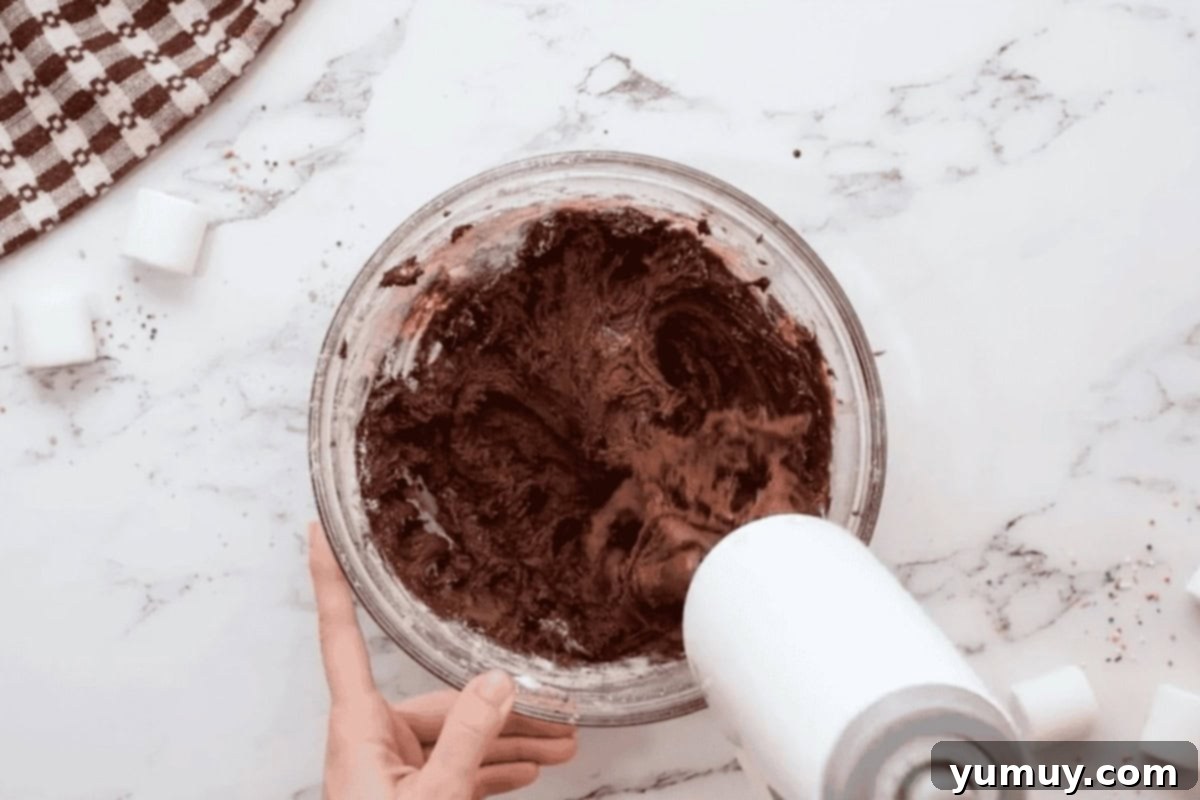 beating hot chocolate cookie dough in a glass bowl with a hand mixer.