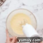 beating sugar, eggs, and vanilla in a glass bowl with a hand mixer.