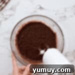 beating wet ingredients for hot chocolate cookies in a glass bowl with a hand mixer.